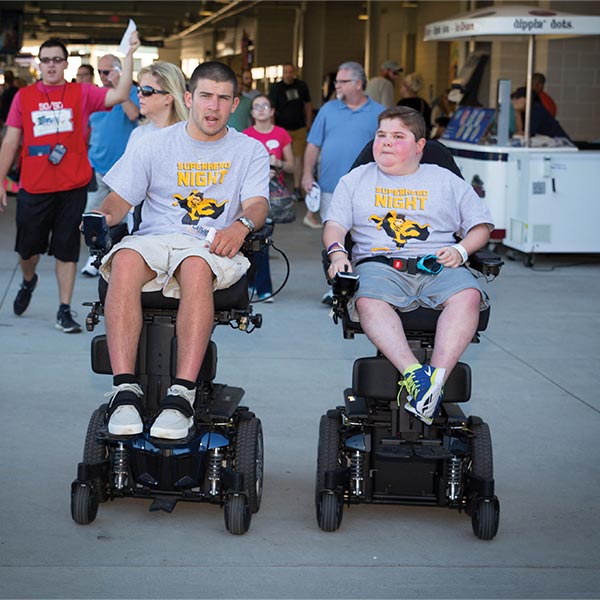 One man and one boy using the J6 Jazzy power wheelchair at a baseball game