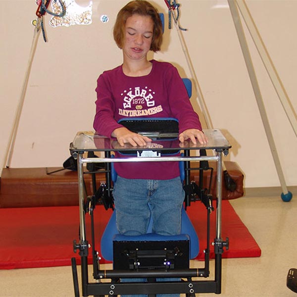 Teenage girl using the Prime Engineering Symmetry Youth Pediatric Standing Frame with the desk attachment