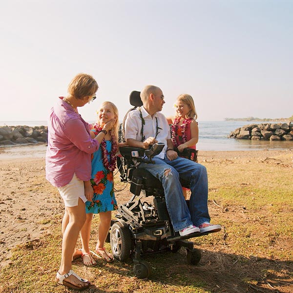 man on beach with family seated in a power wheelchair using the Quantum Q6 Edge 2.0